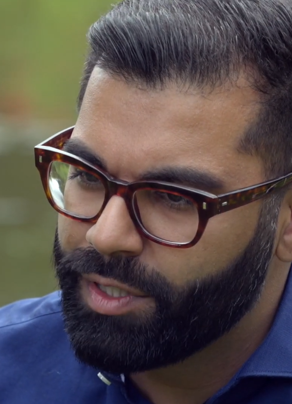 Image of Tarang Chawla, he has a dark beard and tortoiseshell glasses and a blue shirt. He's looking away from the camera and speaking.