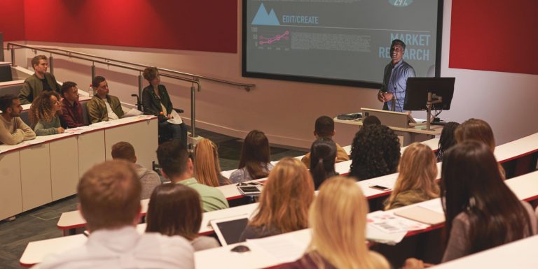 Students sitting in a lecture theatre listening to a lecturer giving a presentation.